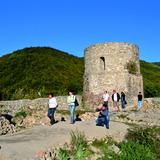 Wieża zamkowa na tle wzgórz, na dziedzińcu spacerujący turyści.