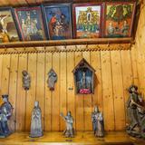 Obrazy na szkle wiszące na ścianie, drewniane rzeźby stojące na półce, kapliczki i świątki.