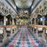 Wnętrze drewnianego kościoła. Szachownicowa posadzka, ławy polichromowane, rzędy kolumn międzynawowych marmoryzowanych z falistymi łukami, w głębi ołtarz.
