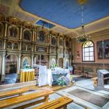 Wnętrze drewnianej cerkwi z ikonostasem, ołtarzem, ławkami.
