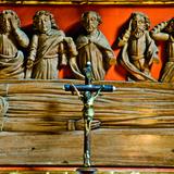 Krzyż, za nim drewniane rzeźby na pomarańczowym tle w kościele p.w. św. Filipa i Jakuba w Sękowej.