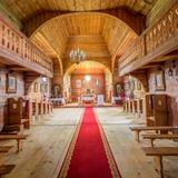 Wnętrze drewnianej cerkwi. Drewniane ściany i ciekawy strop, w oddali ołtarz, po bokach ławki ki na górze galeria dla chóru.