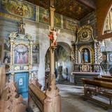 Wnętrze drewnianego kościoła. Widok na boczna ścianę nawy z obrazami i ołtarzem, oraz przejściem do kaplicy.