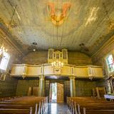 Wnętrze drewnianego kościoła widziane od strony wejścia, na którym znajduje się chór z prospektem organowym. Na suficie widać polichromię, po prawej stronie niewielka drewniana ambona.