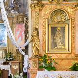 Ołtarz główny i ołtarz boczny w kościele św. Katarzyny w Tenczynku. W ołtarzu bocznym stół przykryty białym obrusem, kwiaty oraz obraz św. Katarzyny na tle brązowego marmuru ze złoconymi ozdobami. Po bokach figury świętych. Po lewej stół przykryty białym obrusem, pod nim kwiaty, za nim kolejny z tabernakulum, z kwiatami, ze świecami po bokach, nad nim obraz Przemienienia Pańskiego na jasnobrązowym tle ze złoceniami i aniołami u góry. Po prawej stronie wisi rollup z wizerunkiem Jezusa. Z sufitu zwisają białe wstążki.