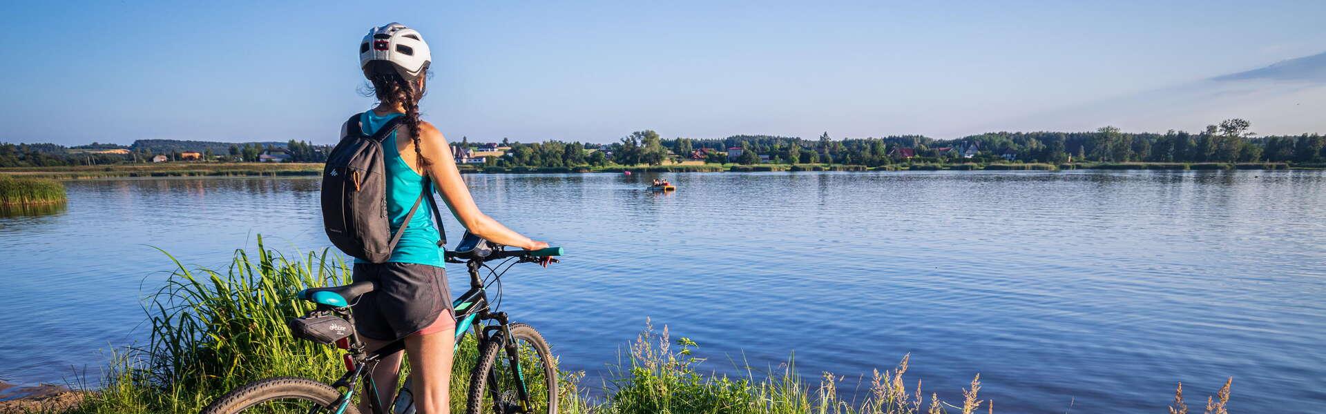 Kobieta na rowerze, odwrócon tyłek patrząca na zalew.
