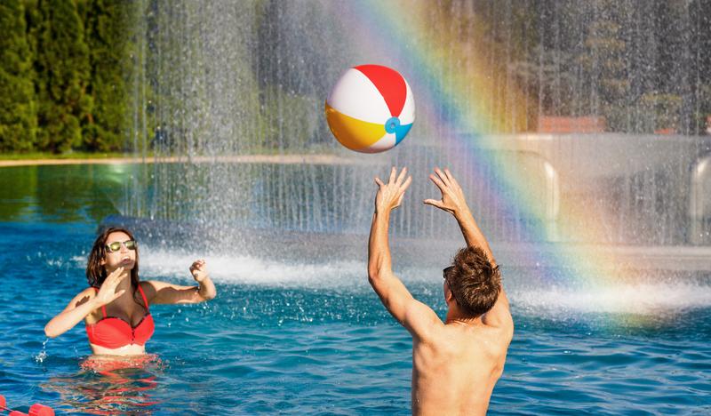 Kobieta i mężczyzna w strojach kąpielowych w basenie, podrzucający piłkę.