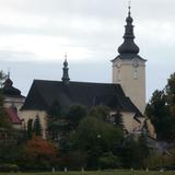 Duży, murowany kościół z wieżą, przysłonięty drzewami.