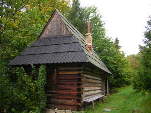 Mały drewniany domek będący Bacówką księdza Józefa Tischnera na Polanie Sumolowej, budowany na zrąb, kryty spadzistym dachem, pośród zielonych drzew.