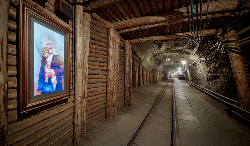 Korytarz w kopalni, na ścianie po lewej stronie wisi portret mężczyzny.