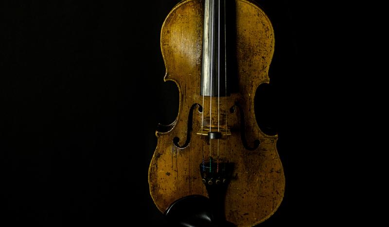 Zdjęcie ukazujące stare skrzypce na smolistym tle.