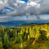 Zdjęcie przedstawiające przepiękny widok na beskid z wieży widokowej eliaszówka. Na pierwszym planie gęsty las w kolorach soczystej zieleni, w głębi liczne pagórki i wzniesienie. W tle rozmywający się horyzont o nieregularnym kształcie. Na niebie przeważa spora ilość chmur.