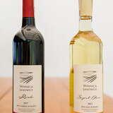 Fotografia ukazuje dwie zakorkowane butelki w których leżakuje wino. W jednej butelce widoczne wino czerwone, a w drugiej wino białe. Oba przygotowane w winnicy Janowice.