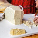 bundz czyli ser z mleka owczego produkowany na Podhalu, który kroi na małe kawałki Pani w stroju góralskim, obok kawałek oscypka