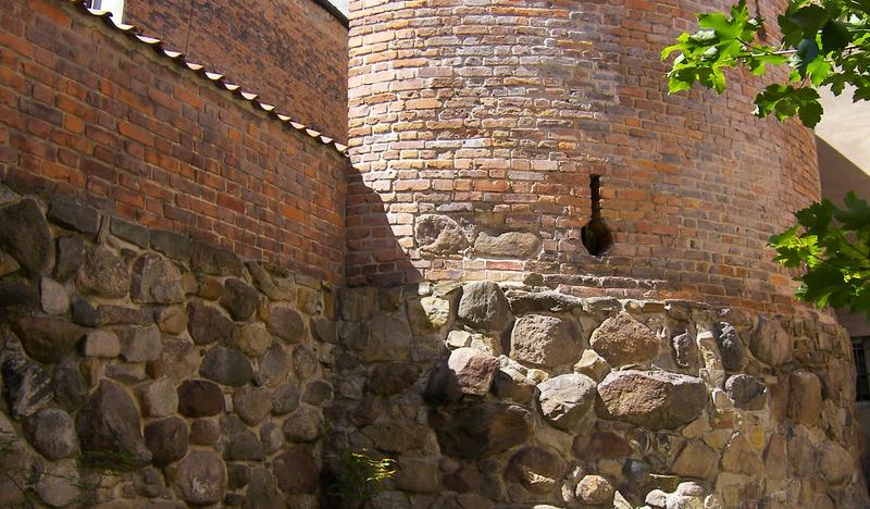 Okrągła baszta z kamienia i cegły z otworami strzelniczymi, przy murach miejskich.