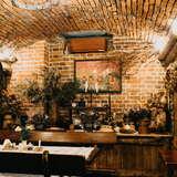 Wnętrze restauracji z cegły, kamienia i drewna. Drewniany stół i łatwy, pod ścianą suszone kwiaty i inne ozdoby.