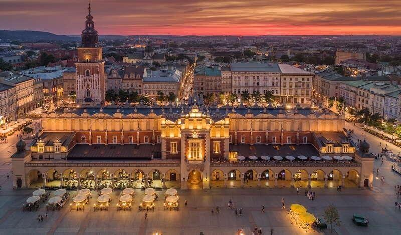 Rozświetlone sukiennice, za nimi kamienice zachodniej części Rynku Głównego oraz widok na Kraków w kolorach zachodzącego słońca