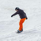Osoba ubrana w strój narciarski zjeżdża po stoku na desce snowboardowej