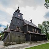 Drewniany, w ciemnym kolorze, kościół z wieżą nad wejściem. Przy kościele ładna zadbana trawa i drzewa. Do kościoła prowadzą kamienne schody.