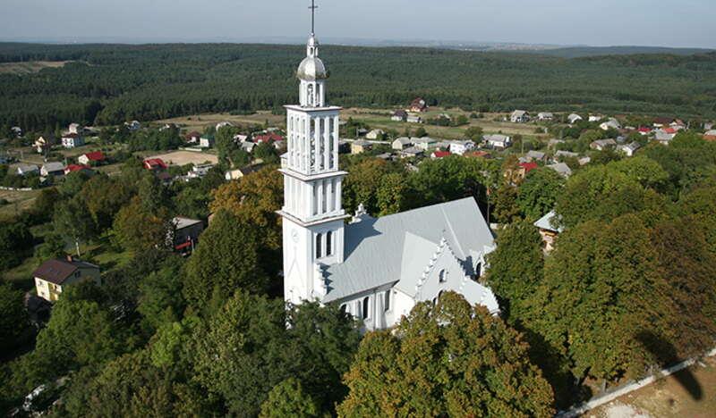 Biały kościół z wysoka wieżą widziany z góry.