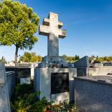 Nagrobki na cmentarzu ustawione blisko siebie, w centralnym punkcie nagrobek z podwójnym krzyżem i czarną tablicą.