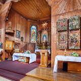 Wnętrze drewnianego kościoła z ołtarzem, amboną i ołtarzami bocznymi.