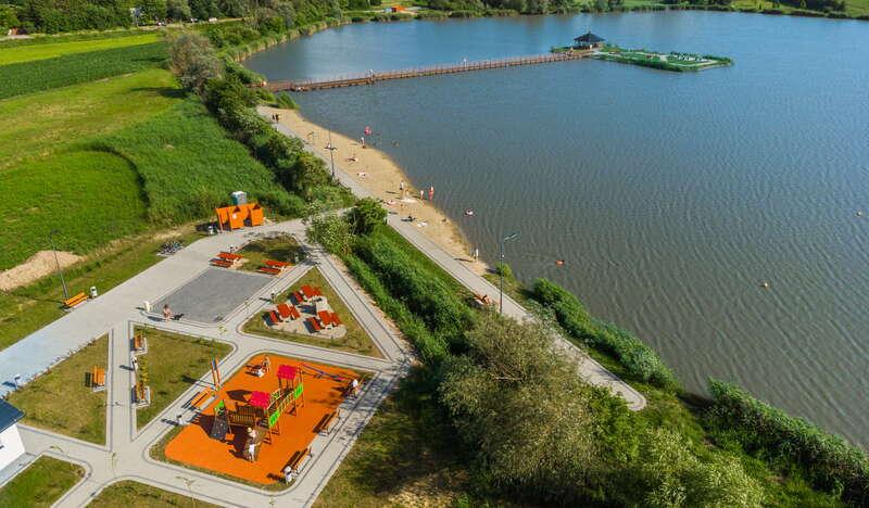 widok na kąpielisko w Januszowicach z lotu ptaka po lewej strefa placów zabaw na środku kąpieliska zadaszona altana do której prowadzi most
