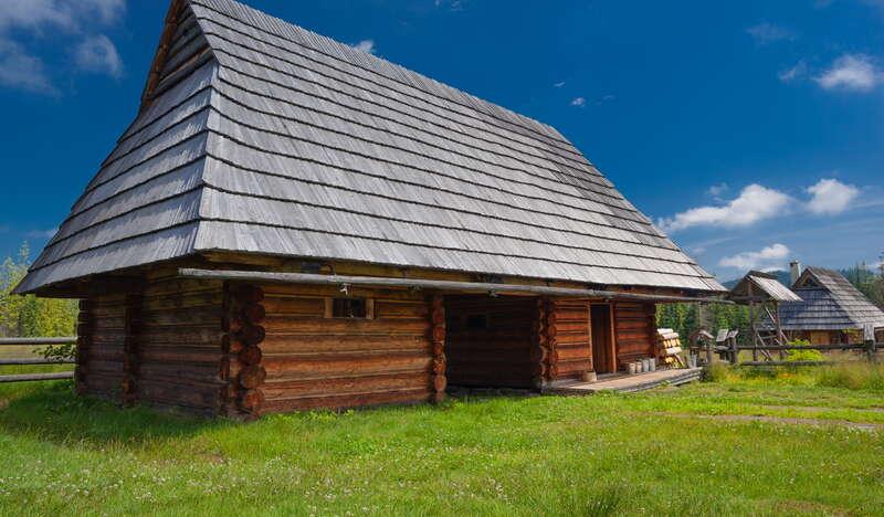 Bacówka Jana Jasionki w Murzasichlu z zewnątrz. Wokół drewnianej chaty rośnie trawa, a nad nią unosi się widnieje niebieskie niebo.