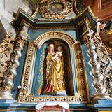 Ołtarz boczny we wnętrzu drewnianego kościoła z figurką Madonny z Dzieciątkiem. Bogato zdobiona rama ze złotymi kolumnami, obok podwieszana ambona ze zdobieniami. Po prawej widoczny sufit z ozdobnymi kasetonami. Po lewej betonowy łuk.