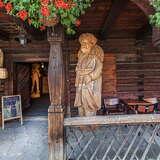 Drewniane rzeźby diabła i mistrza Twardowskiego w podcieniu, przed wejściem do drewnianej karczmy.