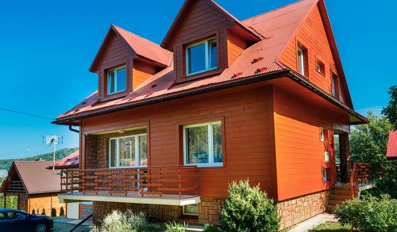 Dom Słoneczko w Wysowej Zdrój z zewnątrz. Dom jest koloru rudego, na podjeździe obok zaparkowane auto, a w tle błękitne niebo.