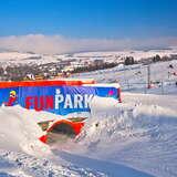 Widok na baner Fun Parku, w tle narciarze na stacji narciarskiej Master Ski Tylicz w zimowy słoneczny dzień