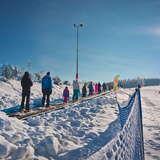 Grupa narciarzy korzystających z przenośnika taśmowego na stacji narciarskiej Master- Ski w Tyliczu, w tle widok na wyciąg krzesełkowy