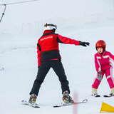 Instruktor uczący dziewczynkę jazdy na nartach na stacji narciarskiej Kokuszka w Piwniczej Zdroju, a w tle wyciąg talerzykowy.