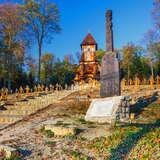 Cmentarz, w dali drewniana kaplica, bliżej pomnik z ciekawym, rzeźbionym obeliskiem.