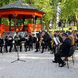 Orkiestra strażacka gra w parku, za muzykami stoi drewniana altana.