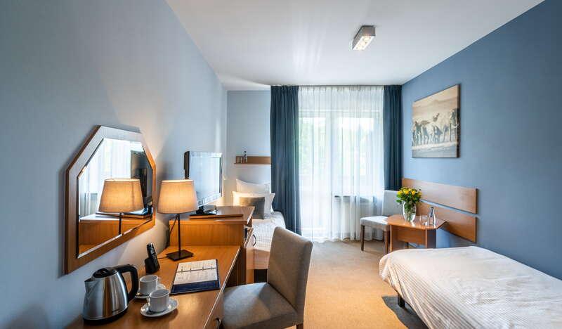 Pokój w hotelu Nawigator w Szczawnicy z dwoma pojedynczymi łóżkami, biurkiem, stolikiem i dwoma krzesłami.