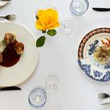 dania elegancko podane na ozdobnych talerzach, pośrodku kielich z żółtym kwiatem, na stole biały obrus