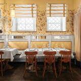 Dwa stoliki na małej sali w Restauracji Kogel Mogel w Krakowie. Ściany na sali są zółte, a stoły nakryte białym obrusem.