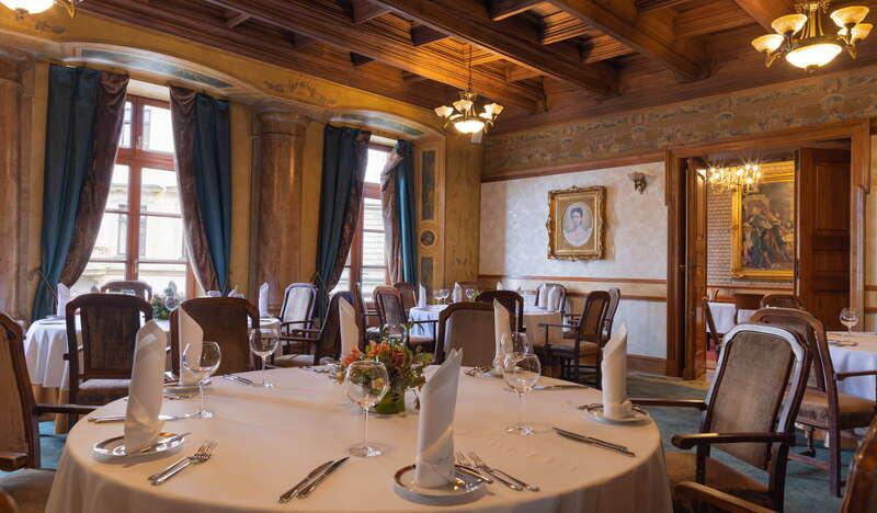 Elegancka sala z przygotowanymi stołami dla gości w Restauracji Wierzynek w Krakowie. Na oknach zasłony, ściany sali ozdobione są marmurowymi kolumnami i malowidłami.