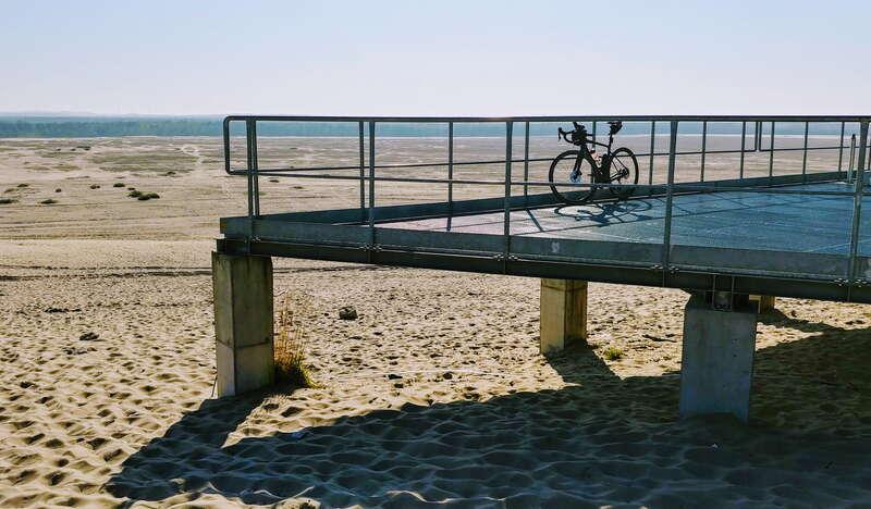 Widok na metalową platformę. widokową, na której zaparkowany jest rower. W tle widok na pustynię Błędowską.
