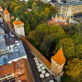 Kawałek murów obronnych w Krakowie widzianych z lotu ptaka. Po lewej widać zabudowania kamienic Starego Miasta, po prawej od murów znajdują się drzewa oraz barbakan.