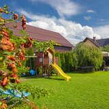 Ogród otaczający budynek, kolorowe kwiaty i krótko przystrzyżona trawa, drewniany domek i żółta zjeżdżalnia dla dzieci.