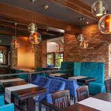 Wnętrze restauracji, stoły drewniane, wokół nich fotele obite pluszem w kolorach niebieskim i turkusowym.