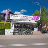 Stoisko wypożyczalni rowerów tuż przy ulicy, charakterystycznych biało-różowo-fioletowy baner reklamowy wypożyczalni