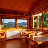 Wnętrze restauracji, ściany z bali, drewniane stoły i krzesła, duże okno z widokiem na Pogórze.