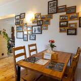 Wnętrze lokalu gastronomicznego, drewniane stoliki i krzesła, na ścianie małe obrazki w drewnianych ramkach.
