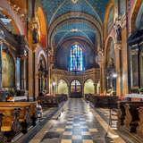 Tylna część Bazyliki św. Franciszka w Krakowie. Po obu stronach kościoła znajdują się mniejsze ołtarze z obrazami, a przy nich drewniane, rzeźbione ławki. Na samym końcu, na środku witraż.