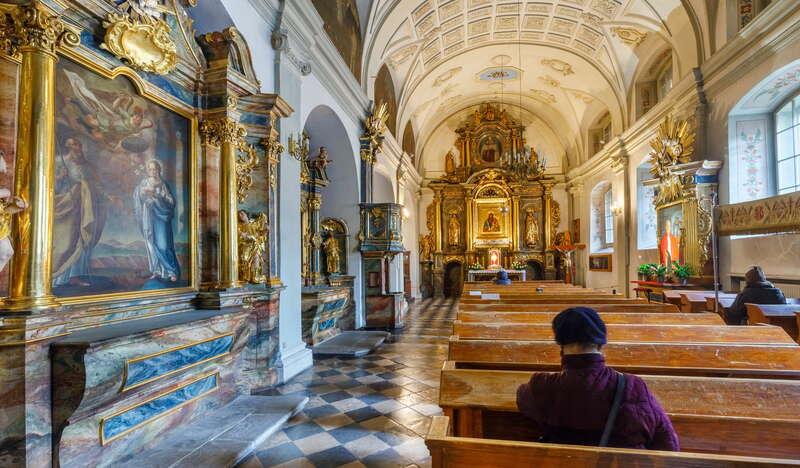 Pomieszczenie w Kościele Nawiedzenia Najświętszej Marii Panny. Ściany zdobią bogate, ozłocone ornamenty oraz marmur. Pośrodku znajduje się rząd drewnianych ławek, a na samym końcu złoty ołtarz.