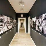 Czarny korytarz w Muzeum Nikifora w Krynicy-Zdroju, Na ścianach wiszą czarno-białe zdjęcia, przedstawiające różnych ludzi.